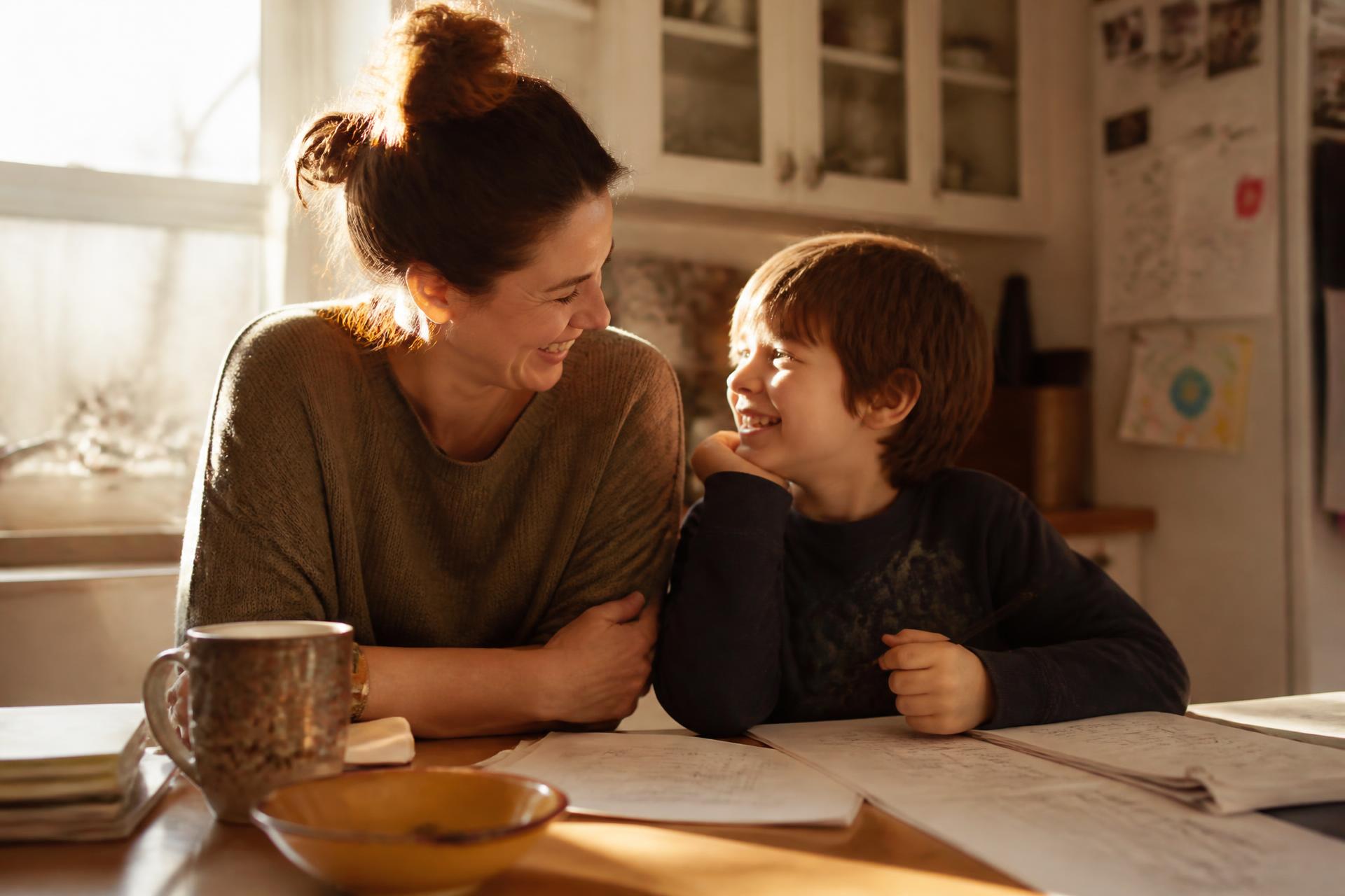 A parent and child laughing together at a sunlit kitchen table